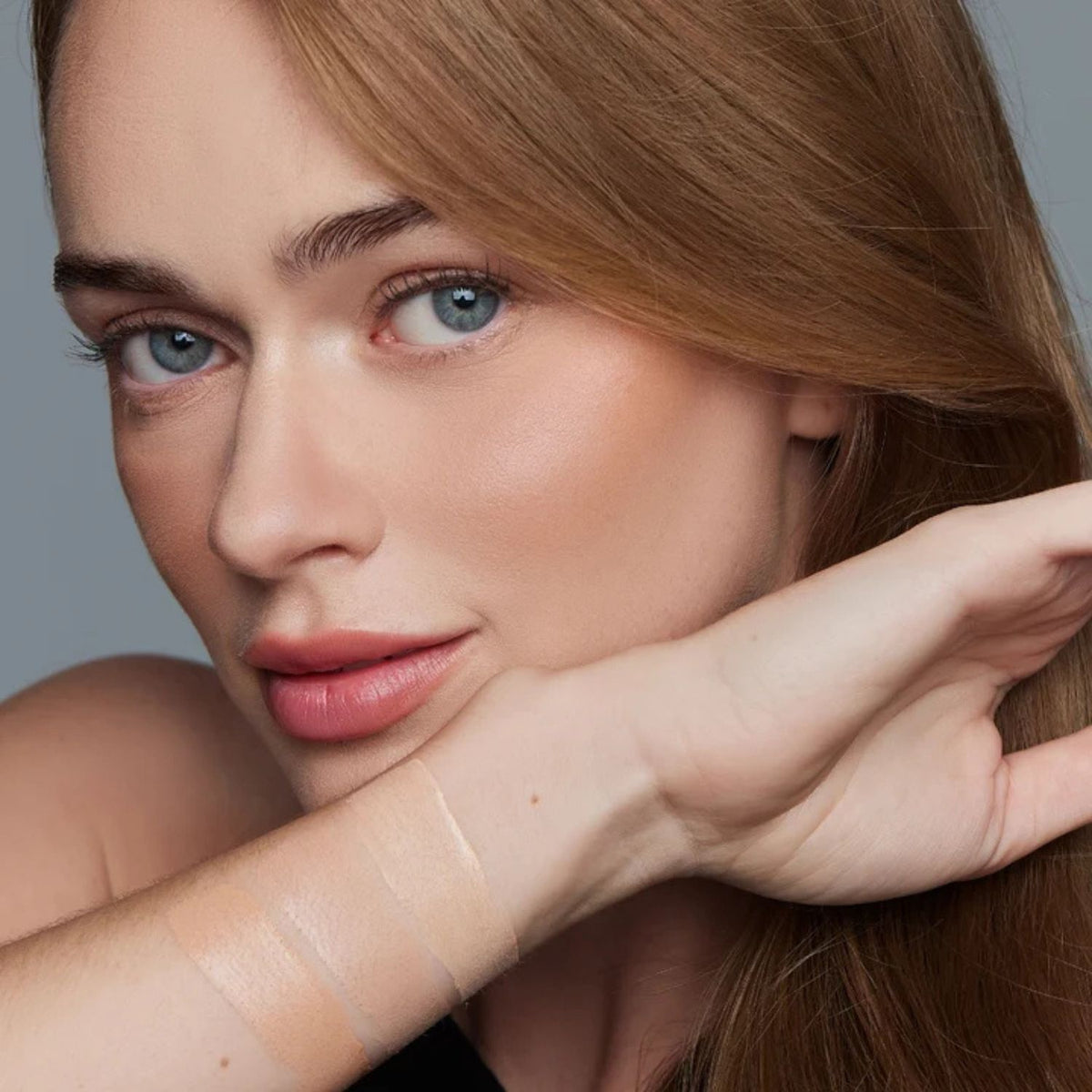 Close-up of a woman with natural makeup, wearing a liquid foundation swatch across her forearm.
